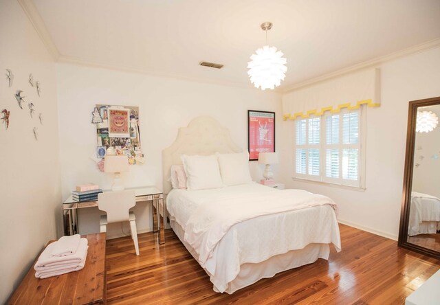 bedroom featuring hardwood / wood-style flooring, crown molding, and a chandelier