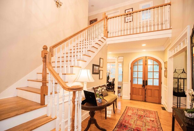 foyer entrance featuring french doors, crown molding, light hardwood / wood-style flooring, and a high ceiling