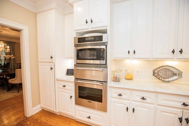 kitchen featuring white cabinets, decorative backsplash, light stone countertops, an inviting chandelier, and light hardwood / wood-style flooring