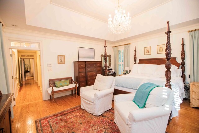 bedroom with ornamental molding, a tray ceiling, light hardwood / wood-style flooring, and a notable chandelier