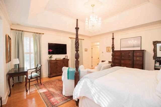 bedroom with a raised ceiling, ornamental molding, hardwood / wood-style floors, and a chandelier