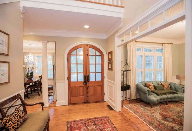 entryway with crown molding, decorative columns, light hardwood / wood-style floors, french doors, and a chandelier