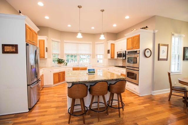 kitchen featuring appliances with stainless steel finishes, a center island, decorative backsplash, and light wood-type flooring