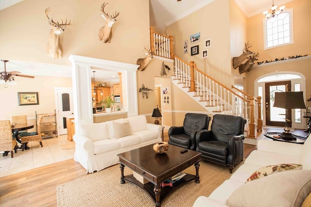 living room with crown molding, a towering ceiling, ceiling fan with notable chandelier, and light wood-type flooring