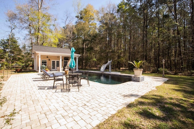 view of swimming pool featuring an outbuilding, a water slide, a patio, and a lawn