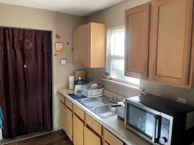kitchen featuring stainless steel microwave, dark wood-type flooring, a sink, light countertops, and a textured ceiling
