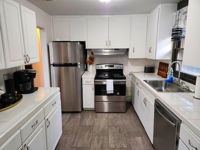 kitchen with appliances with stainless steel finishes, sink, white cabinets, decorative backsplash, and tile counters