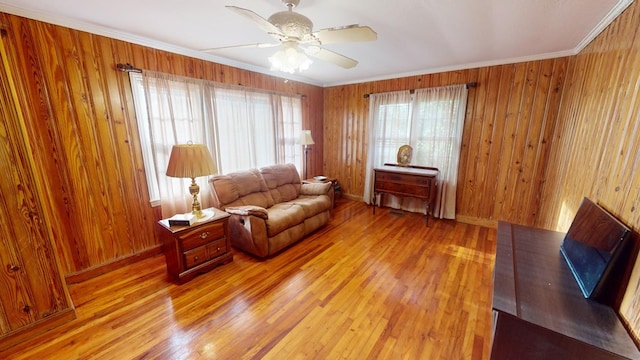 living room with crown molding, light hardwood / wood-style flooring, wooden walls, and ceiling fan