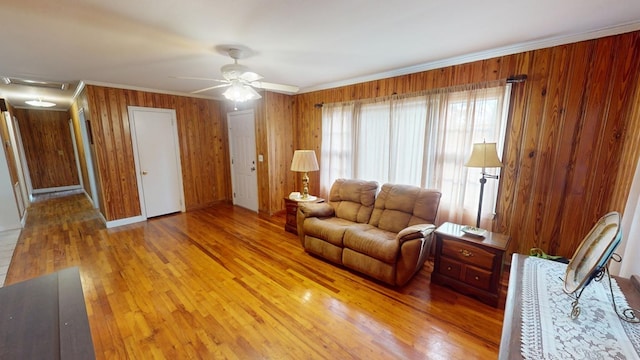 living room with wooden walls, ornamental molding, light hardwood / wood-style floors, and ceiling fan