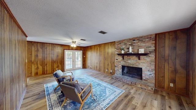 living room with french doors, a fireplace, light hardwood / wood-style flooring, and a textured ceiling