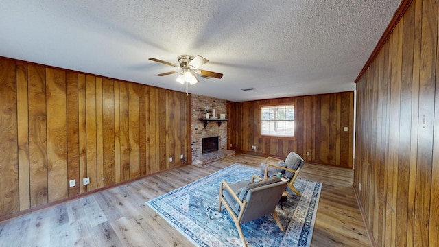 living room featuring a brick fireplace, light hardwood / wood-style flooring, a textured ceiling, and ceiling fan