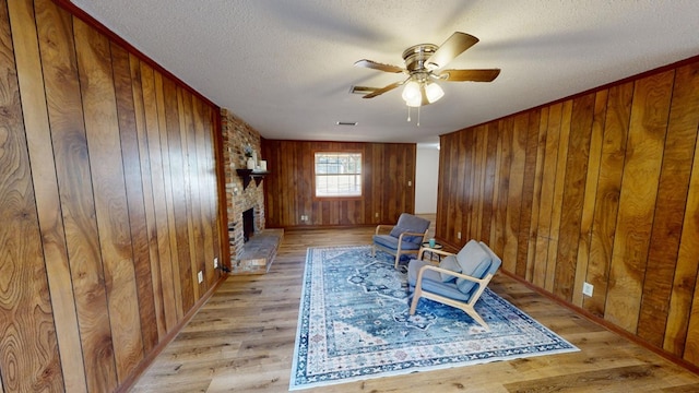 sitting room with a brick fireplace, light hardwood / wood-style flooring, ceiling fan, and wood walls