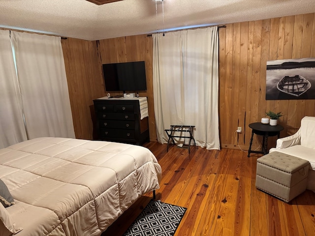 bedroom with wood walls, a textured ceiling, and wood finished floors