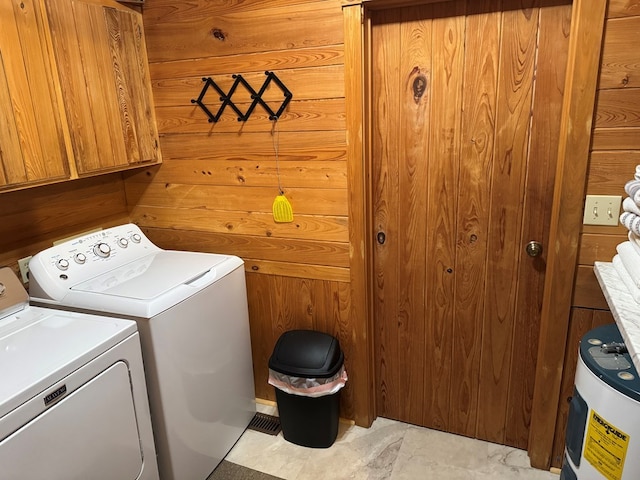 clothes washing area with washer and dryer, wooden walls, cabinet space, and marble finish floor