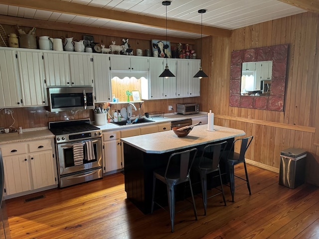 kitchen featuring hardwood / wood-style floors, a sink, light countertops, appliances with stainless steel finishes, and beamed ceiling