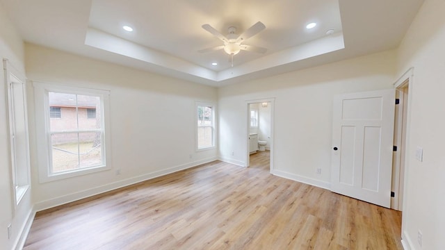 empty room with light wood-type flooring, baseboards, a tray ceiling, and recessed lighting