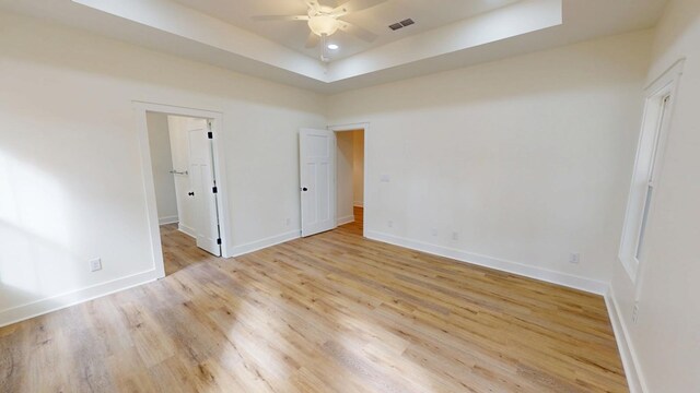 unfurnished bedroom with light wood-style flooring, recessed lighting, visible vents, baseboards, and a tray ceiling