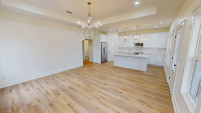 kitchen featuring a center island with sink, appliances with stainless steel finishes, decorative light fixtures, light countertops, and white cabinetry