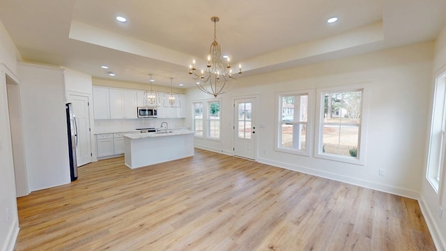 kitchen featuring a tray ceiling, pendant lighting, appliances with stainless steel finishes, white cabinets, and a kitchen island with sink