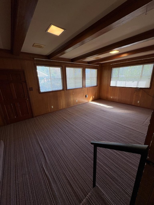 carpeted spare room with beam ceiling, wooden walls, and visible vents