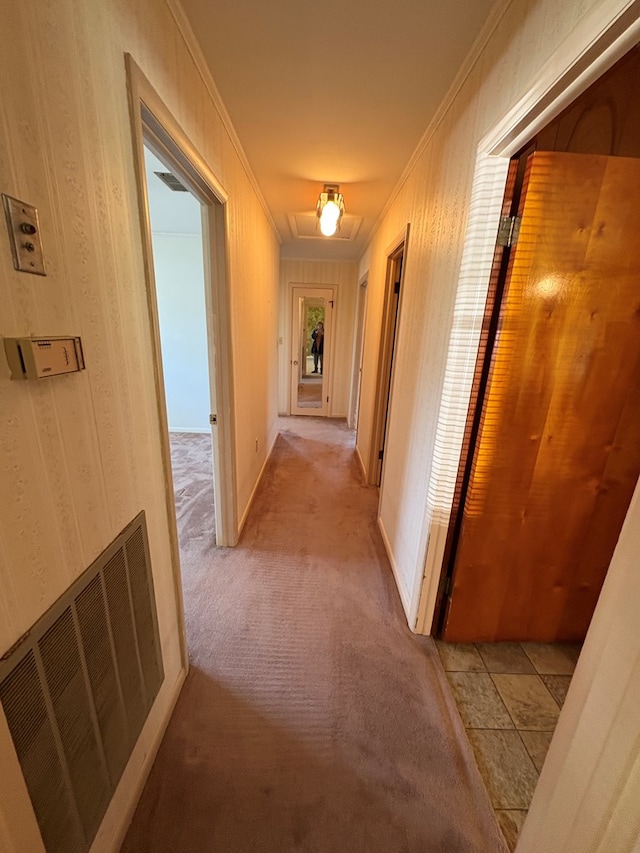 corridor with baseboards, ornamental molding, visible vents, and light colored carpet