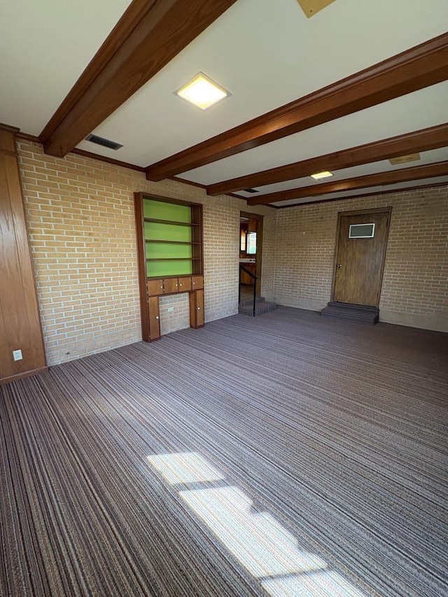spare room featuring beamed ceiling, carpet flooring, and brick wall