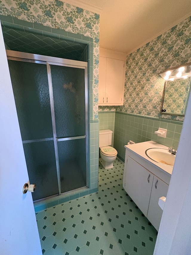 full bathroom with wallpapered walls, a shower stall, tile walls, and wainscoting