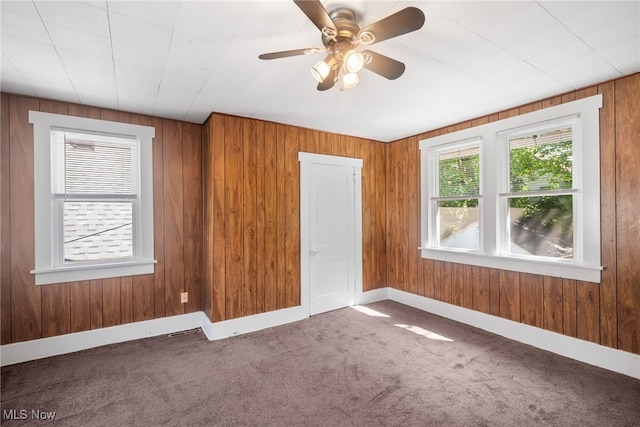 carpeted spare room featuring ceiling fan and wooden walls