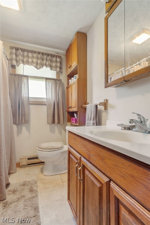 bathroom with vanity, tile patterned floors, toilet, baseboard heating, and a textured ceiling