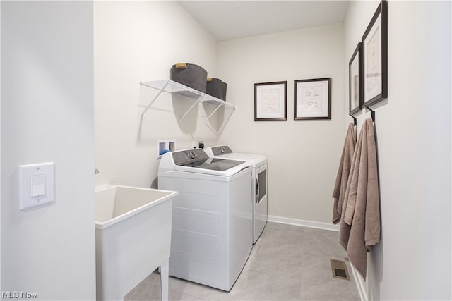 clothes washing area with washing machine and clothes dryer, sink, and light tile patterned floors