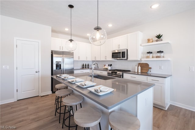 kitchen with backsplash, a center island with sink, light wood-type flooring, and stainless steel appliances