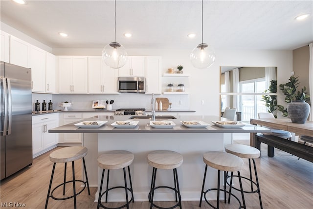 kitchen with appliances with stainless steel finishes, a center island with sink, sink, hanging light fixtures, and light wood-type flooring