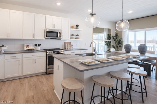 kitchen with appliances with stainless steel finishes, backsplash, light wood-type flooring, and a kitchen island with sink