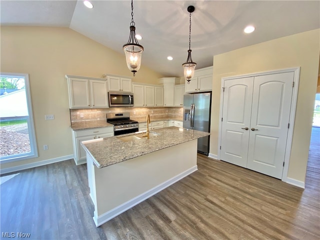 kitchen with pendant lighting, vaulted ceiling, white cabinetry, appliances with stainless steel finishes, and hardwood / wood-style floors