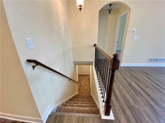 staircase with baseboards, visible vents, arched walkways, and wood finished floors