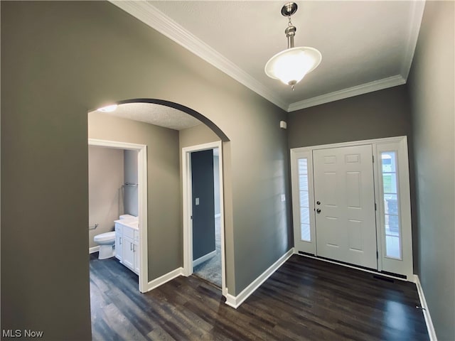 entrance foyer featuring arched walkways, ornamental molding, dark wood-style floors, and baseboards