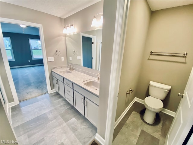 bathroom with toilet, a sink, baseboards, and double vanity