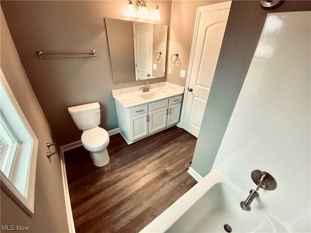 bathroom with a tub to relax in, wood-type flooring, vanity, and toilet