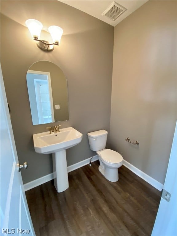 half bathroom featuring baseboards, visible vents, toilet, wood finished floors, and a sink