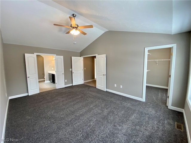 unfurnished bedroom featuring lofted ceiling, dark colored carpet, visible vents, a spacious closet, and baseboards