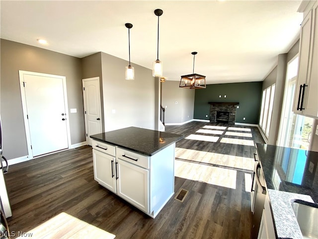 kitchen with dark stone counters, dark wood-type flooring, white cabinetry, a kitchen island, and a stone fireplace