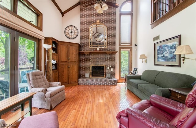 living room featuring a brick fireplace, light hardwood / wood-style floors, high vaulted ceiling, and ceiling fan