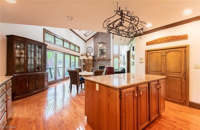 kitchen with a brick fireplace, light stone counters, ornamental molding, vaulted ceiling, and a kitchen island