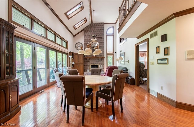 dining room featuring a brick fireplace, light hardwood / wood-style flooring, high vaulted ceiling, and ornamental molding