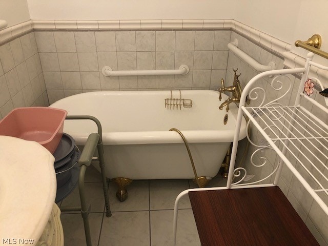 bathroom with a tub to relax in, tile walls, toilet, and tile patterned floors