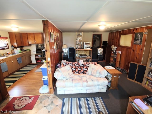 living room with light wood-type flooring, wooden walls, and sink