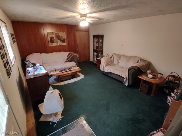 carpeted living room featuring ceiling fan, wood walls, and a textured ceiling