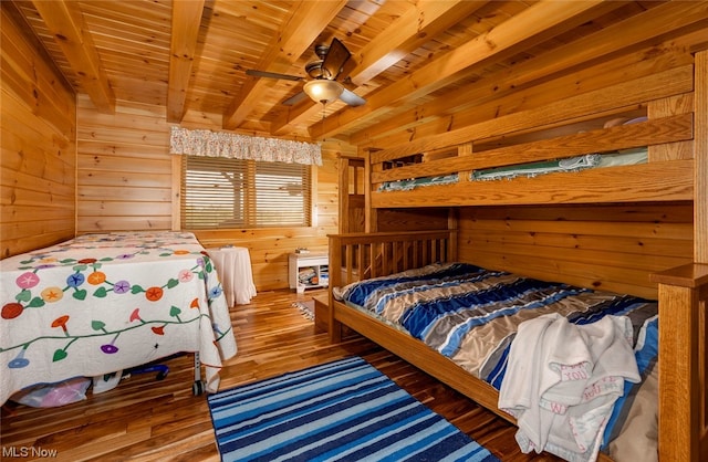 bedroom with beamed ceiling, wood-type flooring, wood ceiling, ceiling fan, and wooden walls