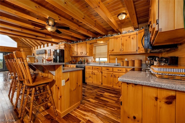 kitchen with wood walls, dark hardwood / wood-style flooring, black appliances, a center island, and ceiling fan