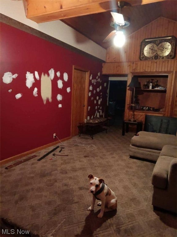 unfurnished living room featuring wood walls, beamed ceiling, ceiling fan, and carpet flooring